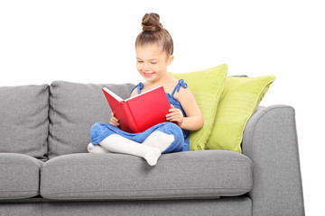 Little girl reading a book seated on sofa