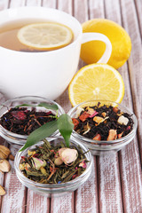 Cup of tea with aromatic dry tea in bowls on wooden background