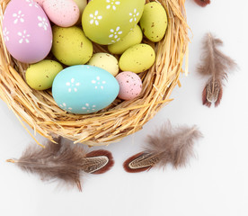 Easter eggs in nest and decorative feathers, isolated on white