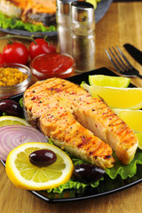 Tasty grilled salmon with lemon and vegetables, on wooden table