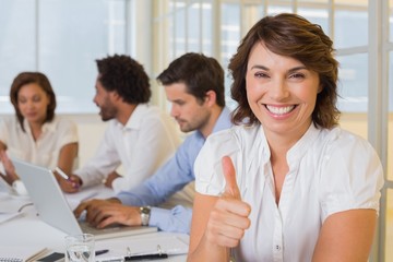Smiling businesswoman gesturing thumbs up with colleagues in
