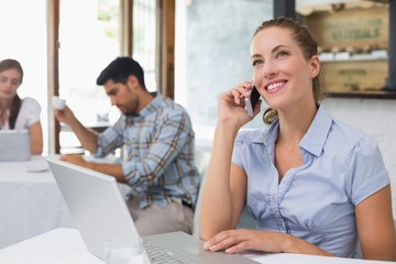 Woman using laptop and mobile phone in coffee shop