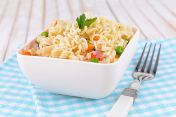 Tasty instant noodles with vegetables in bowl on table close-up