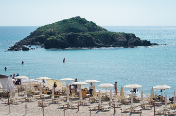 Tropical beach with deckchairs, umbrellas and people.