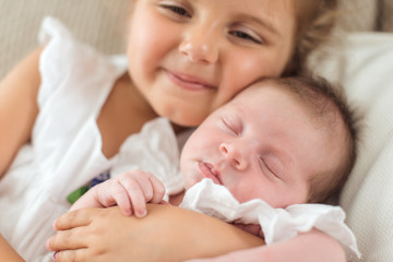 Obraz na płótnie Canvas Newborn girl in a christening dress in her sister arms