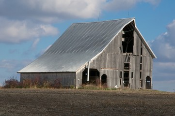 Fototapeta na wymiar Decaying Barn in Barren Field with Blue Sky