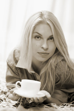 Woman lying at the bed and drinking coffee.