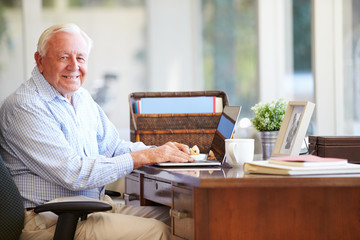 Senior Man Using Laptop On Desk At Home
