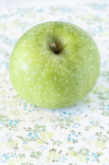 Close up of a green apple on a flowered tablecloth
