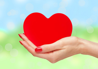 Red heart in woman hands over bright nature background