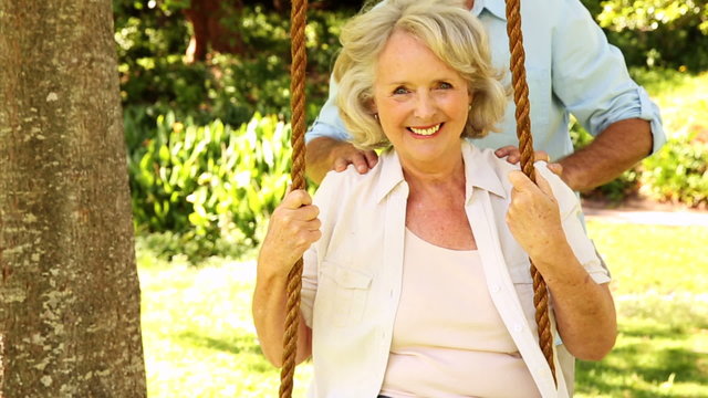 Retired man pushing his wife on swing