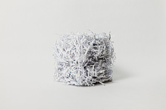A cube made of shredded office paper is lit from one side against a clean off-white background.