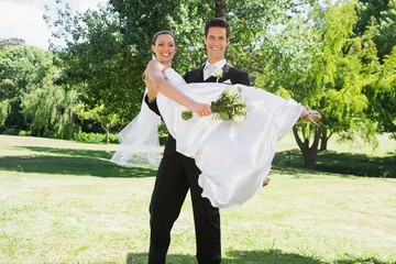 Young groom lifting bride in arms at garden