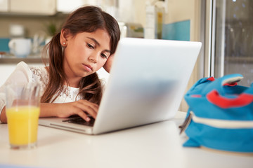 Unhappy Hispanic Girl Using Laptop To Do Homework At Table