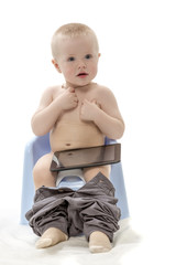 The kid sits on chamberpot and the tablet computer looks