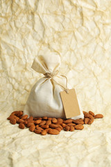 Fototapeta na wymiar Almonds in sack with tag on old paper background