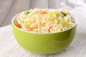 Tasty instant noodles with vegetables in bowl on table close-up