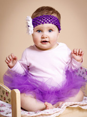 Beautiful little baby in tutu skirt sitting in bed.