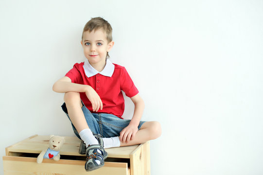 Little Boy Sitting On The Dresser In The Red Shirt.