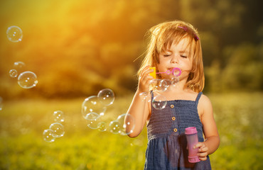 little girl blowing soap bubbles in nature