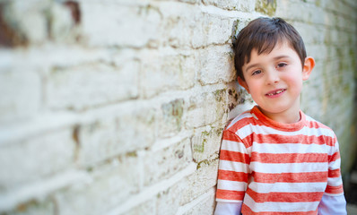 Cute happy boy leaning against brick wall