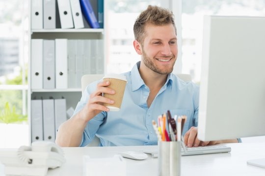 Smiling man working at his desk drinking a take away coffee