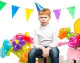 Funny little redhead boy among birthday balloons