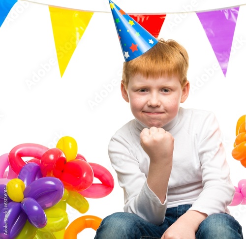 Funny little redhead boy among birthday balloons
