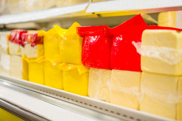 Huge brick form pieces of cheese in color packs on shelves in su