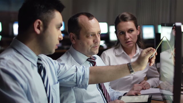 Three white-collar workers discussing computer project in office