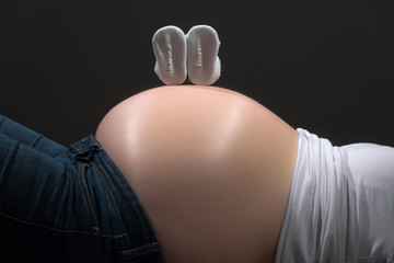 Pregnancy belly with little blue shoes isolated on grey. Close-u