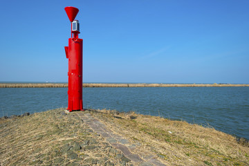 Red beacon on a dike in a lake under a clear sky