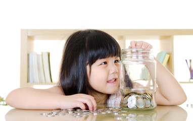 Obraz na płótnie Canvas Little girl putting coins into the glass bottle.