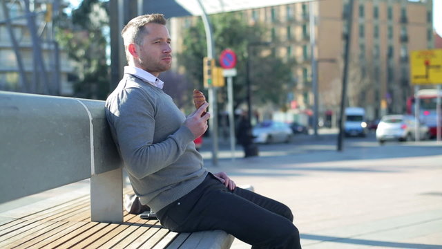 Man sitting on street bench and eating croissant.
