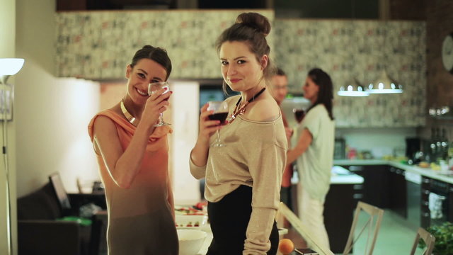 Female friends smiling cheers wine to camera at party couple bac