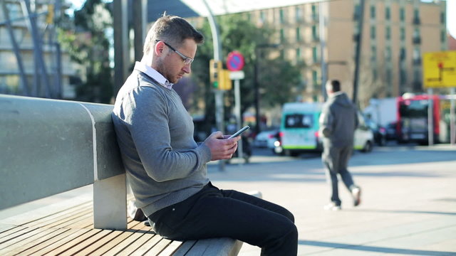 Man sitting on street bench and using cellphone