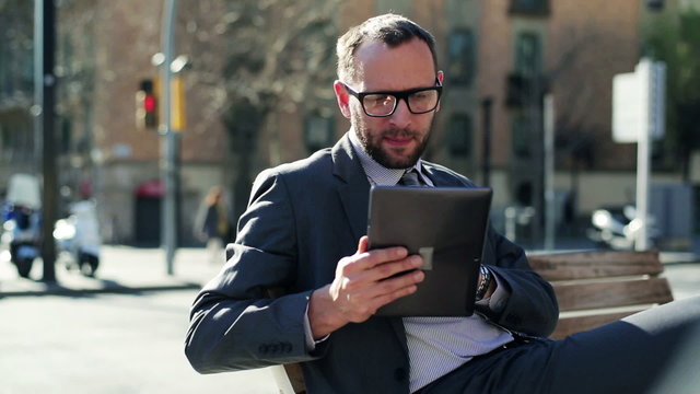 Businessman working on tablet and sitting on street bench, stead