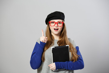 Girl at glasses and beret holds tablet pc and holds finger up