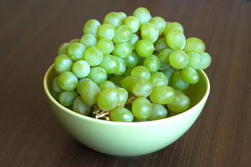 Grape in branch in green bowl on dark table surface