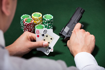 Man Playing Poker While Holding Gun