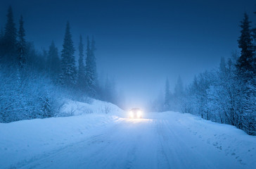 Fototapeta premium lights of car and winter road in forest