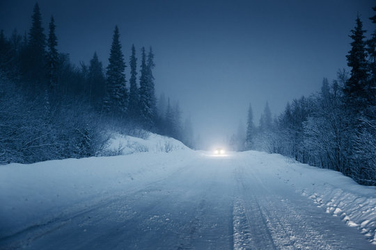 Fototapeta lights of car and winter road in forest