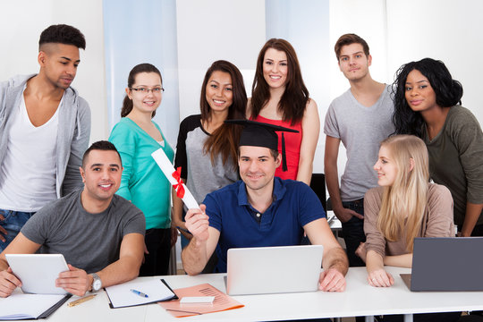 College Student Holding Degree With Classmates Looking At Him