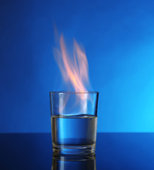 Glass with burning alcohol on blue background