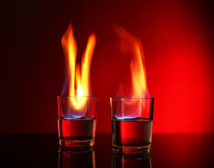 Glasses with burning alcohol on red background