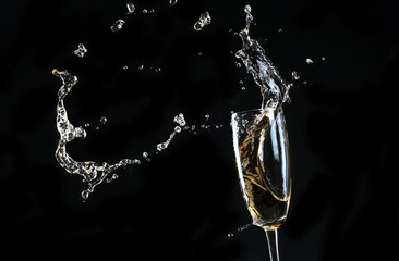 Glass of champagne with splash, on black background