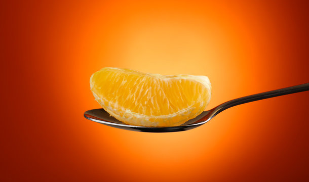 Slice of orange in silver spoon on  orange background