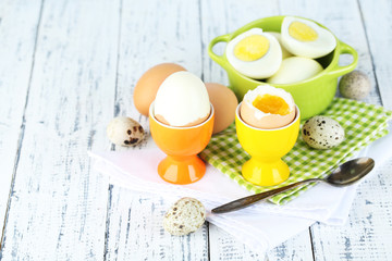 Boiled eggs in pan and eggcup on color wooden background