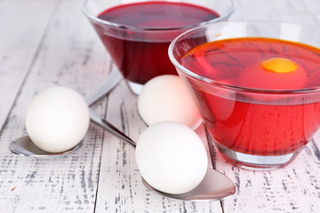 Eggs with liquid colour in glass bowls on wooden background