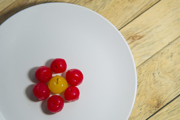 Yellow cherry in group of red cherry on white plate